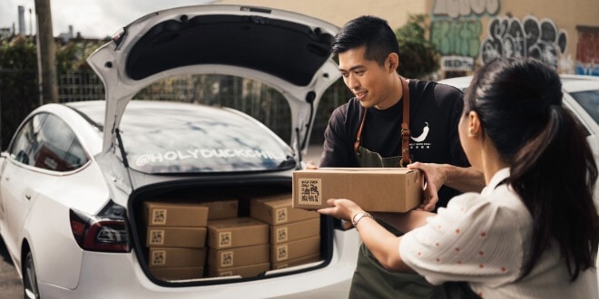 Two Holy Duck Chili employees loading car with boxes of their specialty chili sauce for delivery.