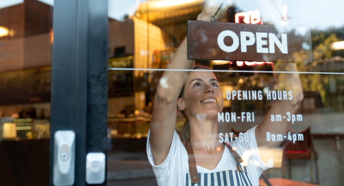 Happy small business owner changing the 'Open' sign on the door of a coffee shop after using QuickBooks to help get started