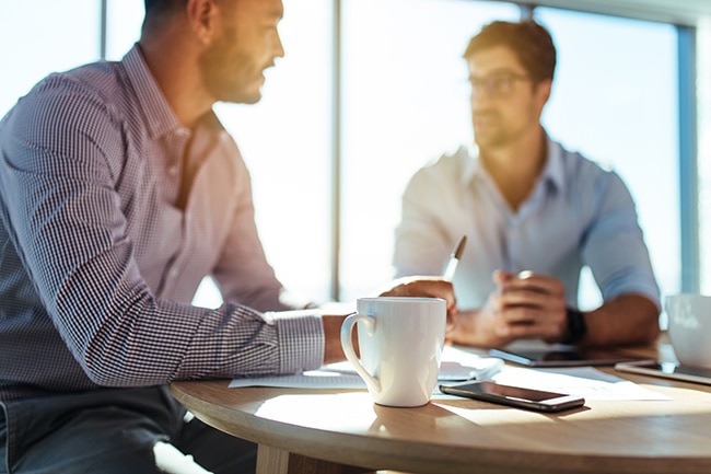 Business executives discussing work at office. Closeup of coffee cup with blurred image of two businessmen sitting on table.