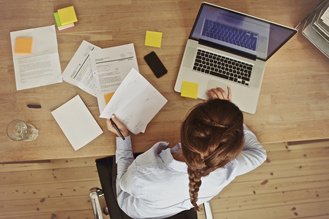 High angle view of an young brunette working at her office desk with documents and laptop.
