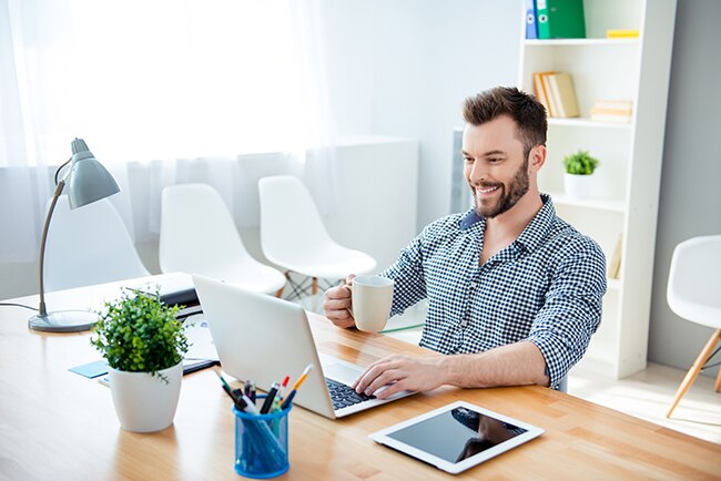 Young happy businessman drinking coffee while working on laptop