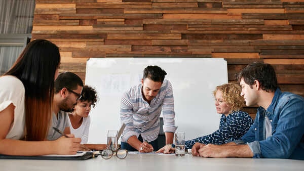 A group of people sitting around a table with laptops.