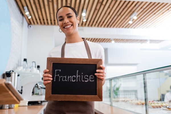 A person smiles as she stands in front of a wooden table.