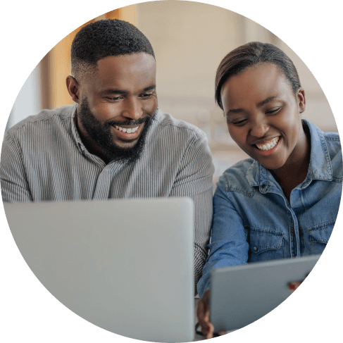 A woman and man looking at a tablet and laptop screen.