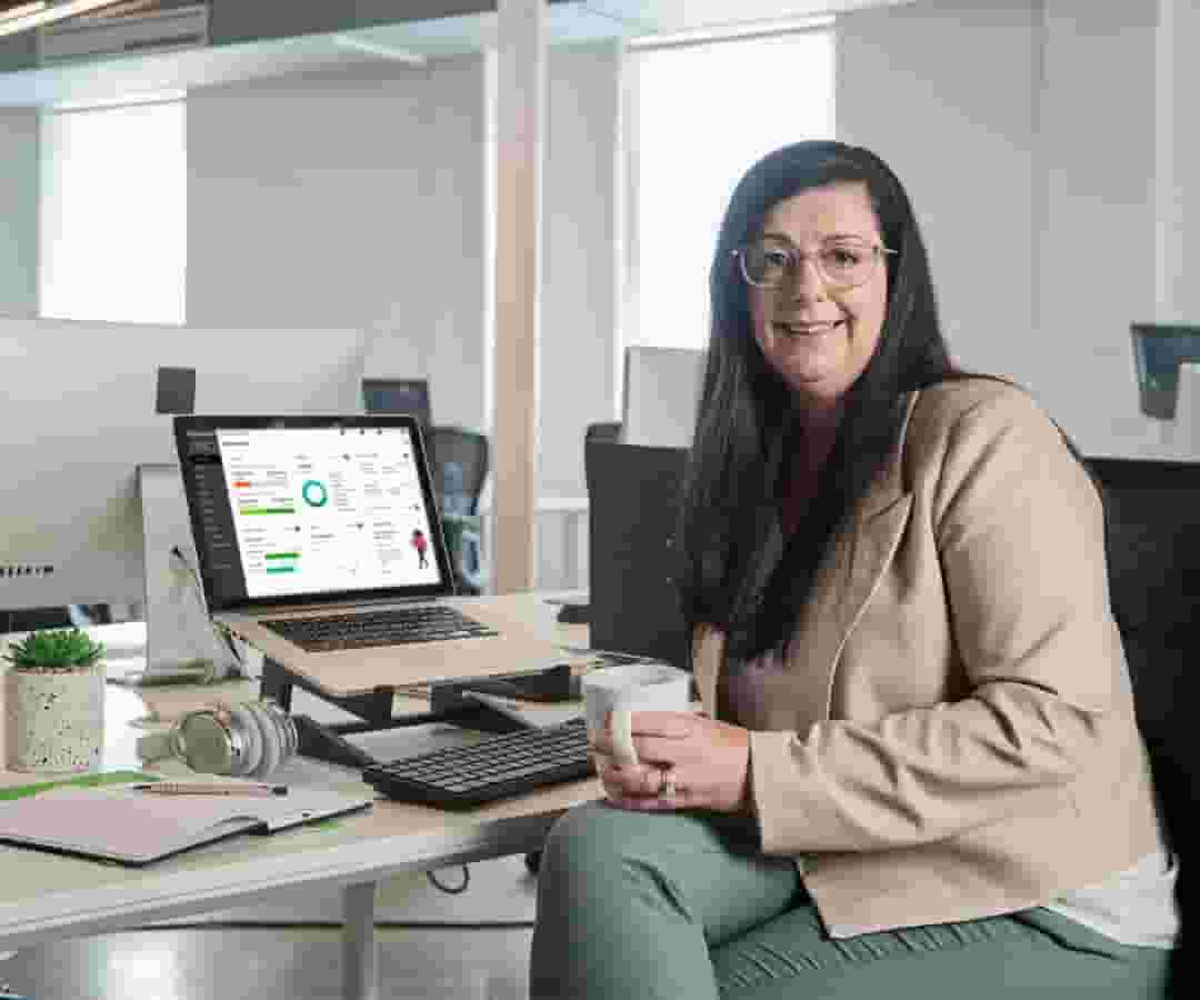 A happy accountant seated at desk with QuickBooks dashboard on laptop in background