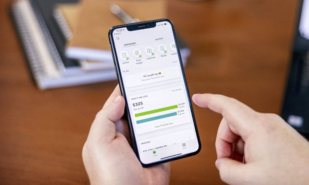 Person holding smartphone displaying QuickBooks dashboard