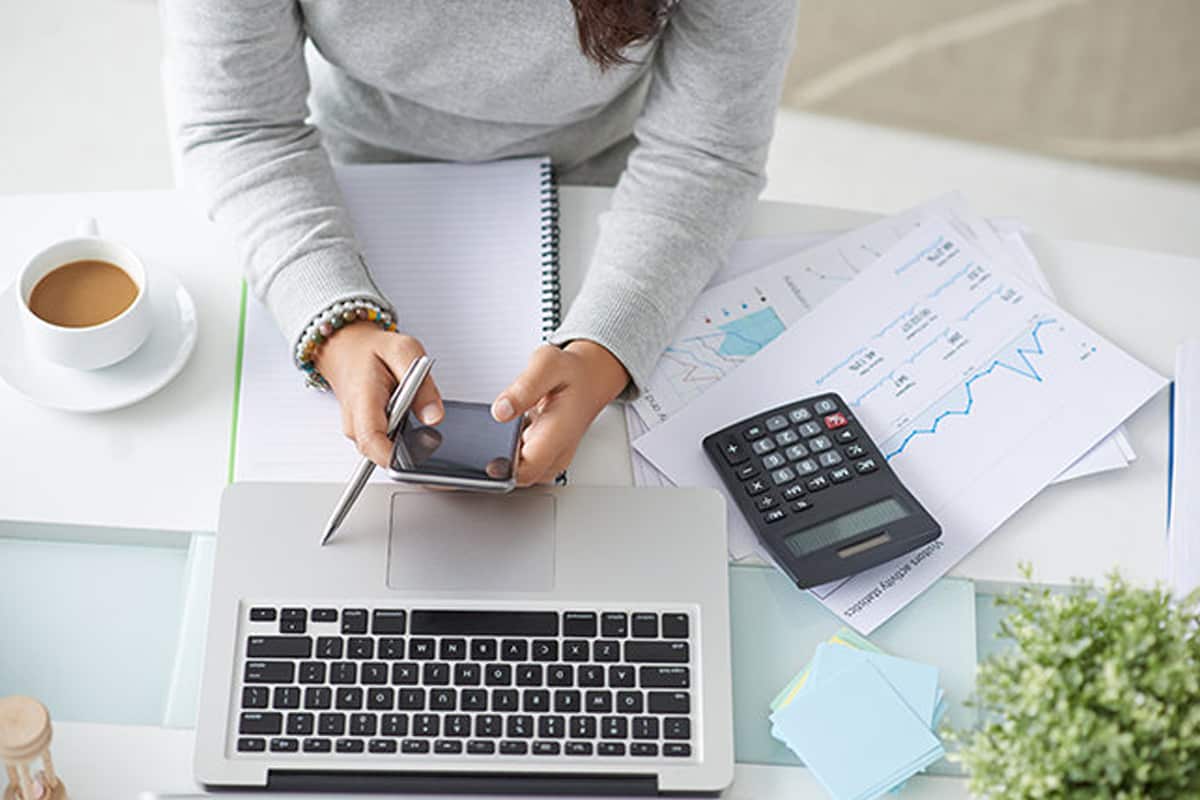 A person sat at a desk using their phone with laptop