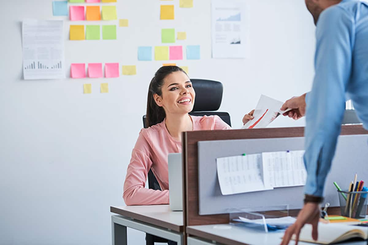 Two employees handing over a document while at desks