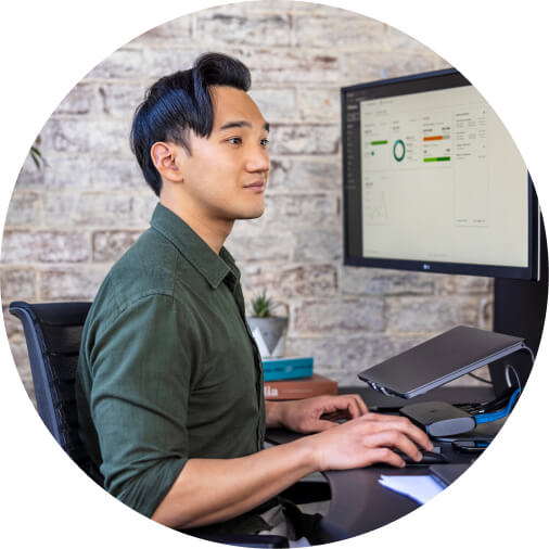 Accountant seated at desk using QuickBooks, with dashboard displayed on computer screens