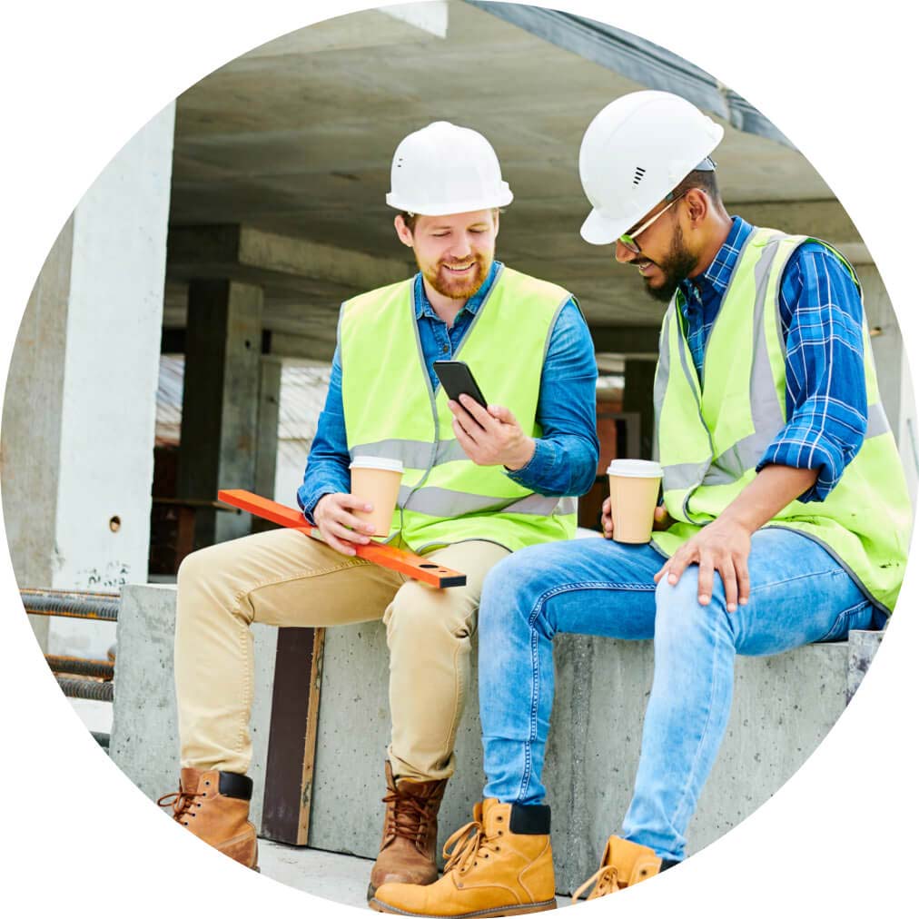 Two tradesmen sitting on site, using QuickBooks app on a mobile phone to estimate job costs