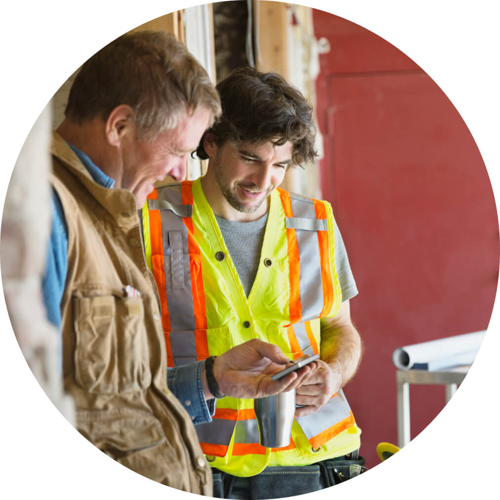 Two happy tradesmen on site, using QuickBooks app on a mobile phone to view payroll