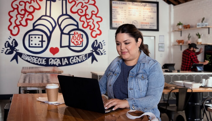 Woman in a coffee shop using QuickBooks on laptop to create and track expenses