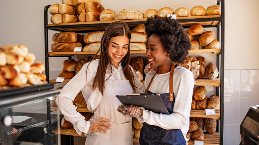 Two ladies standing next to each other and looking at a notepad 