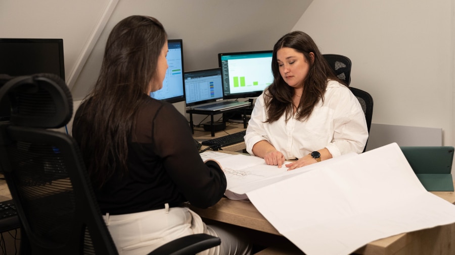 Two women sitting at a desk in front of a computer.