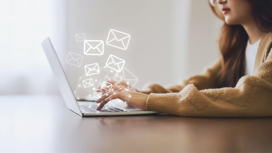 A woman typing on a laptop with email icons coming out of the screen. 