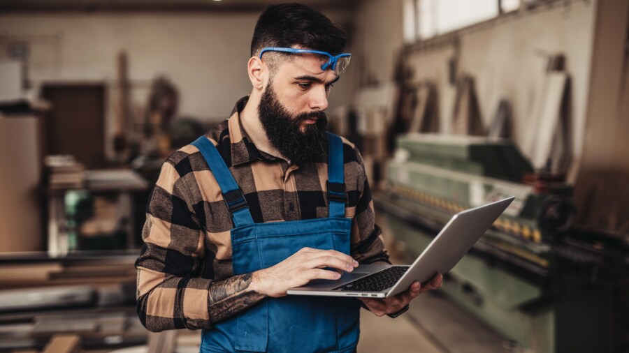 A person in blue overalls looking at a laptop.