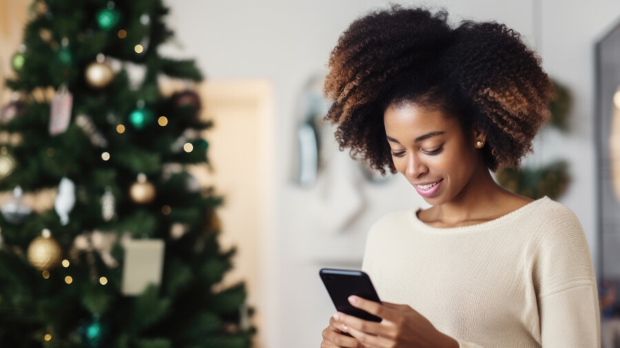 A woman looking at her cell phone next to a Christmas tree.