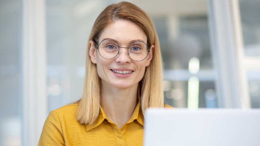 A woman with glasses is sitting in front of a laptop.