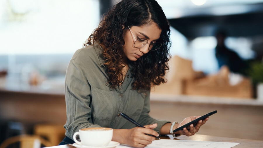 A woman is looking at her mobile phone and writing on a piece of paper