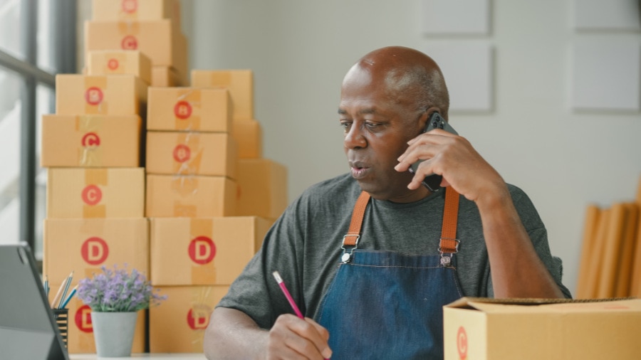 An older gentleman person talking on a phone while recording order in front of a laptop.