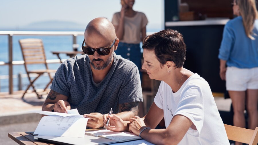 Two people sitting  at a table looking at paper documents 