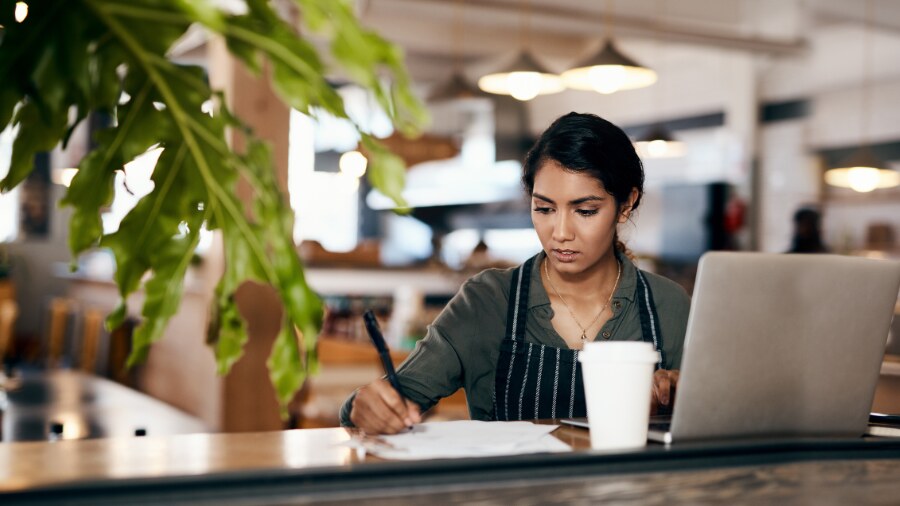 A woman is sitting at a table with a cup of coffee, writing on a piece of paper