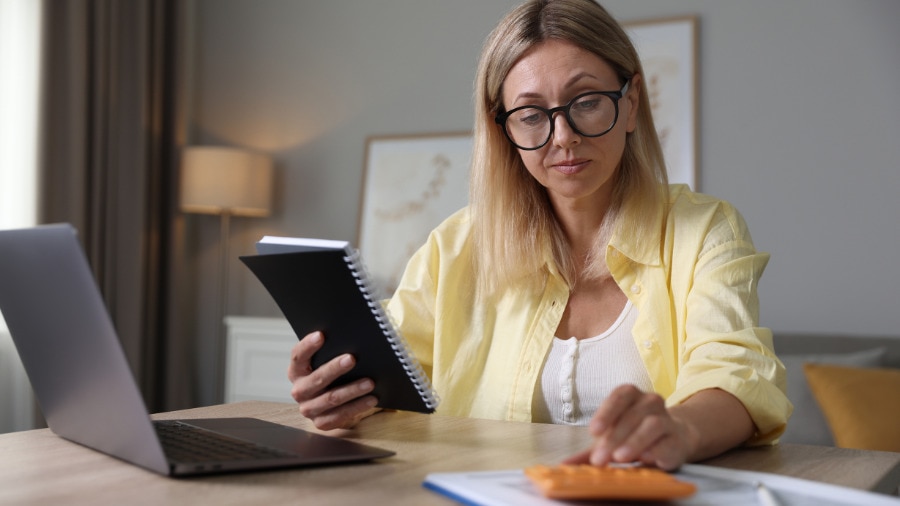 A woman sitting at a desk with a laptop and a book.