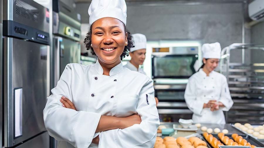 Catering owner and chef smiling while her employees prepare bread rolls in the background
