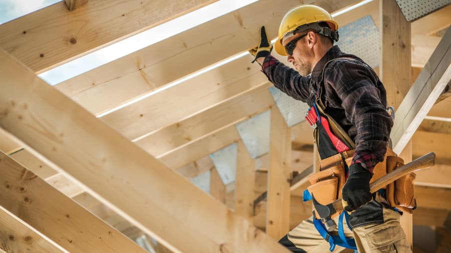 A construction worker walks on wood beams of a building under construction.