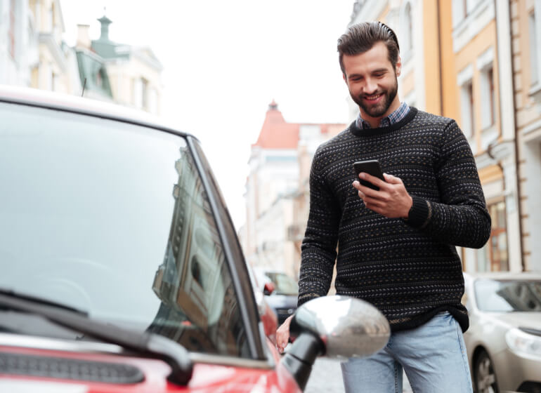 A smiling man looks at his smartphone as he walks up to his car.