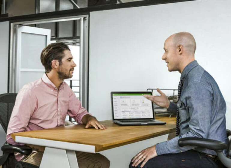 two business men discuss with laptop open