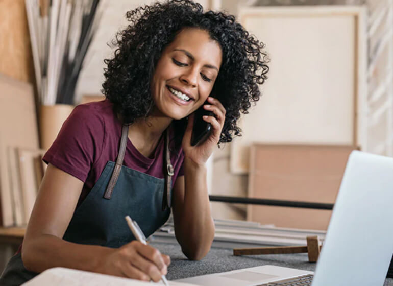 Small business owner smiling, answering a phone call and taking notes.