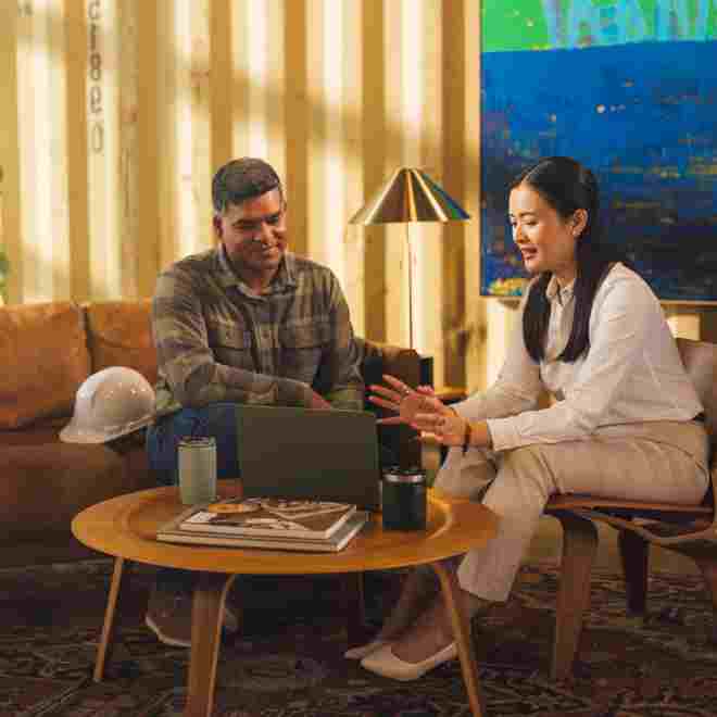 An advisor reviews files with a construction client over a laptop in a relaxed setting.