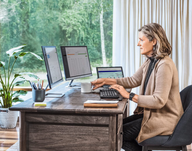 Accountant working at desk with keyboard and three monitors showing Intuit product interfaces