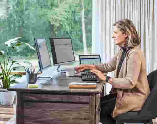  Comptable au bureau naturellement éclairé avec trois moniteurs et un clavier.