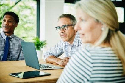 A team at a boardroom table listen intently to a trainer off screen.