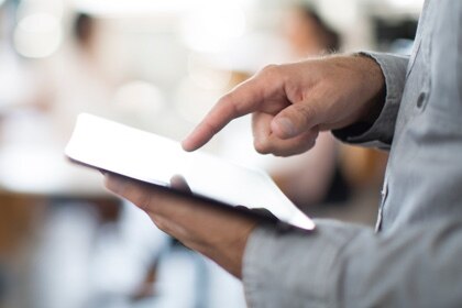 A man's finger pointing at a tablet held in his left hand.