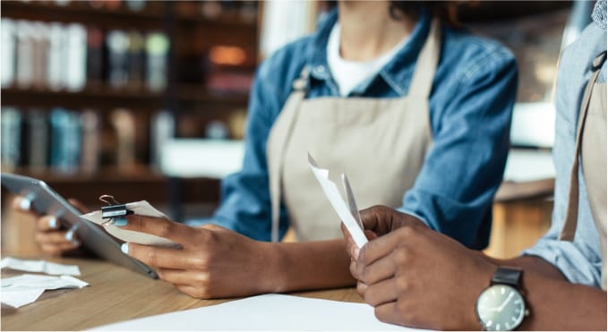 Closeup of two seated workers in aprons checking receipts