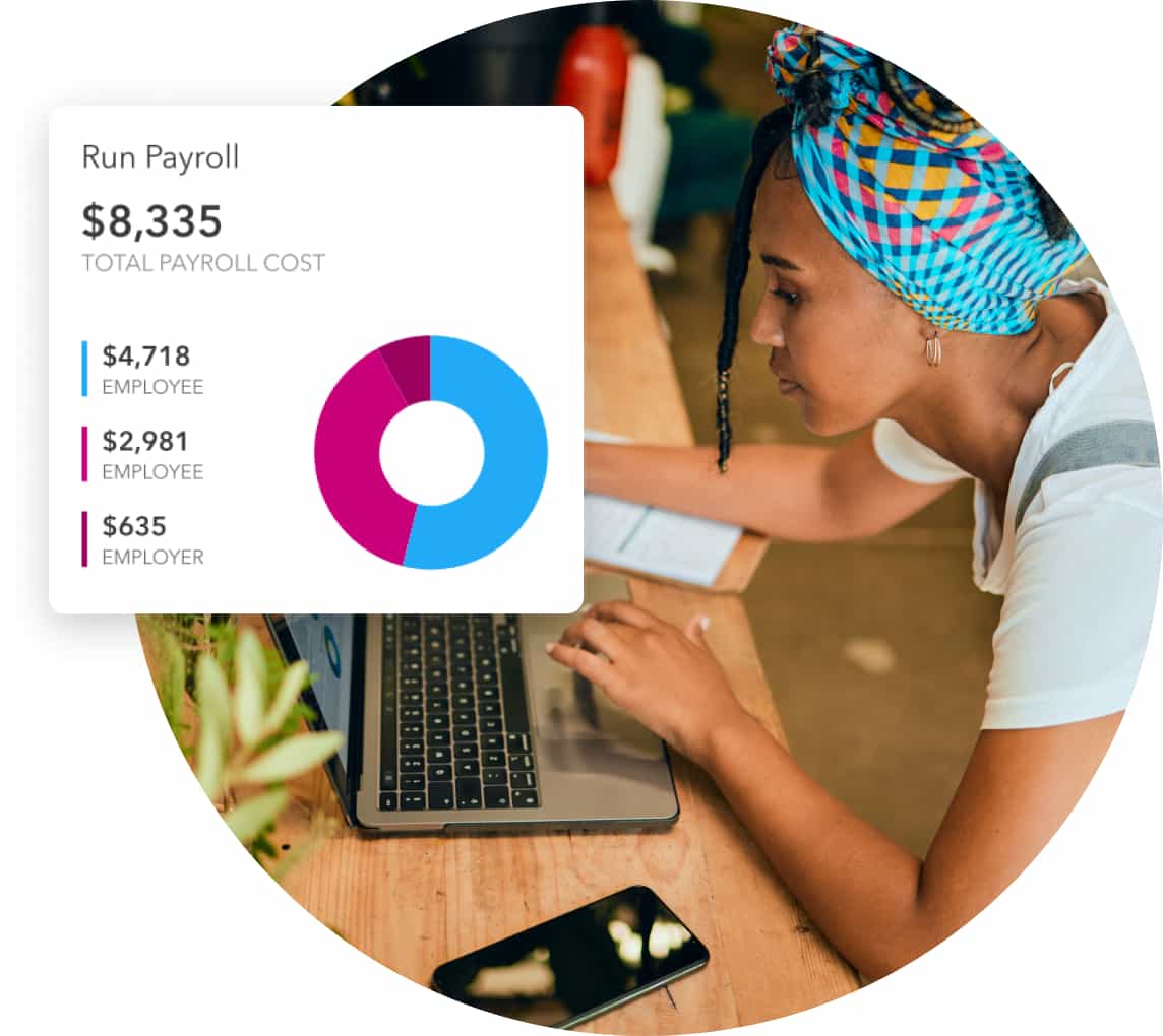 A woman wearing a colourful headscarf checks payroll in QuickBooks on her laptop.