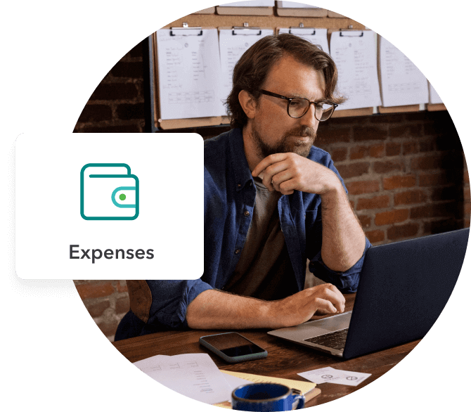 A business owner works on his laptop at a desk. A pop-up shows an expenses icon.