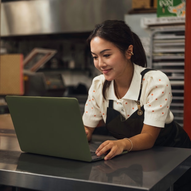 Food industry Asian girl with an apron contacting support using the laptop.