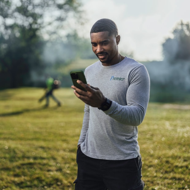 Landscaping company owner standing in the grass checking payroll with mobile.