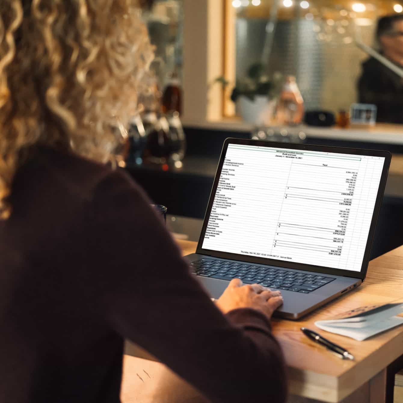 A person sitting at a table with a laptop, viewing spreadsheet.