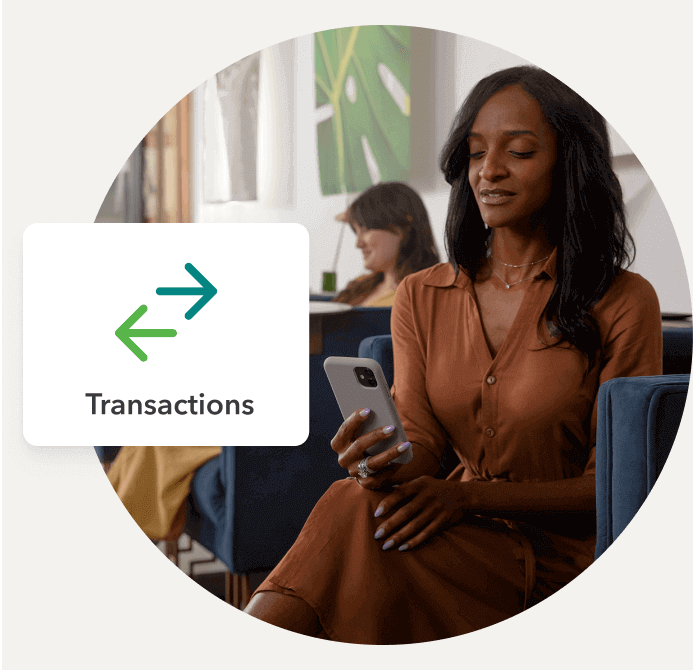 A woman looks at her smartphone in a lounge. A pop-up shows a transactions icon.