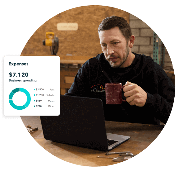 A business owner sips coffee at his laptop in a workshop. A QuickBooks Online Dashboard shows his expenses.