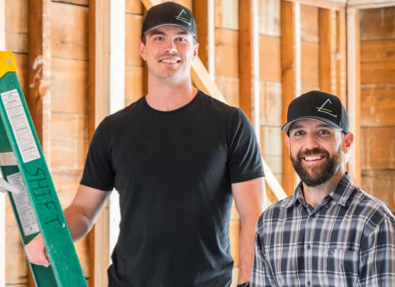 Two men in work clothes stand in a home extension that’s under construction.