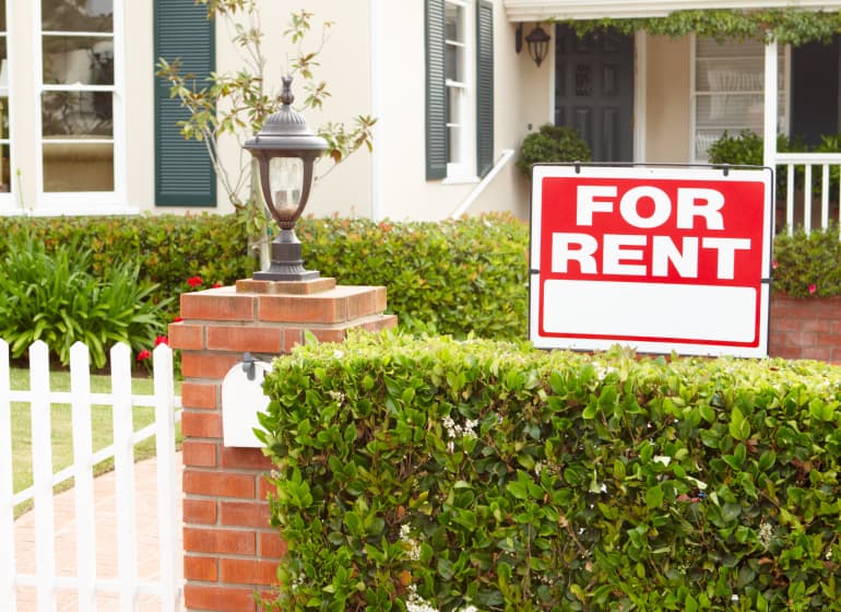 A for rent sign outside a white bungalow. 