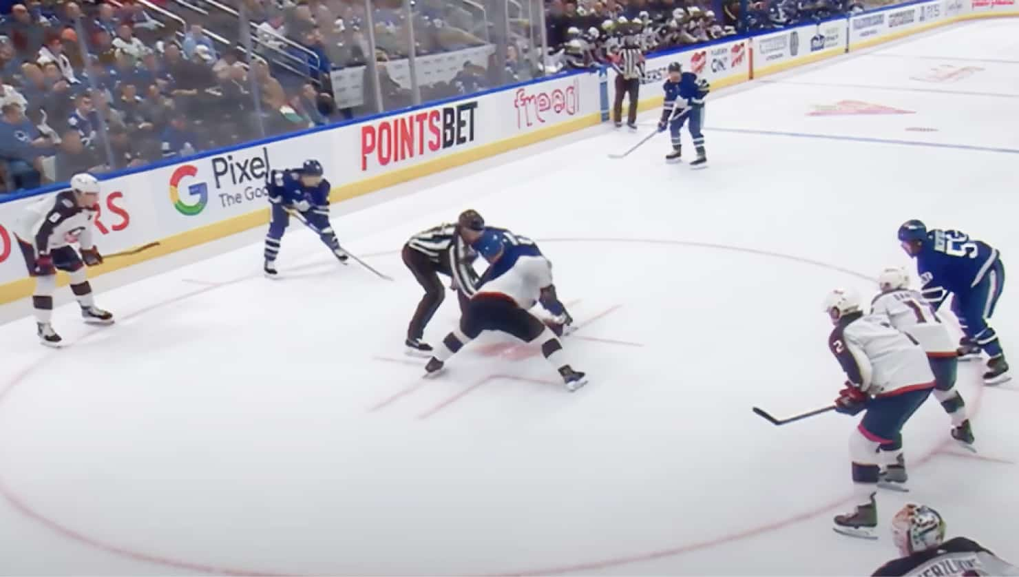 NHL hockey players face off while a large crowd eagerly watches.