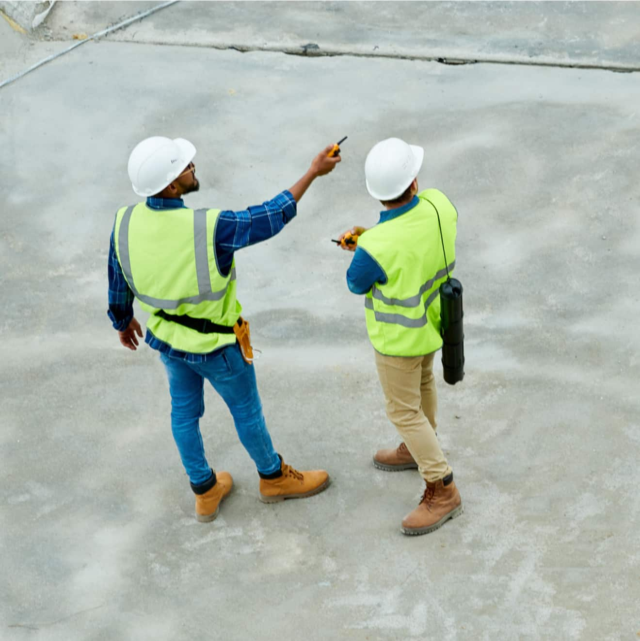 Top view portrait of two workers standing on concrete floor of construction site and planning project.