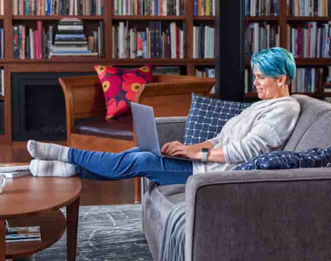 Relaxed woman on couch, working on laptop, with her feet up